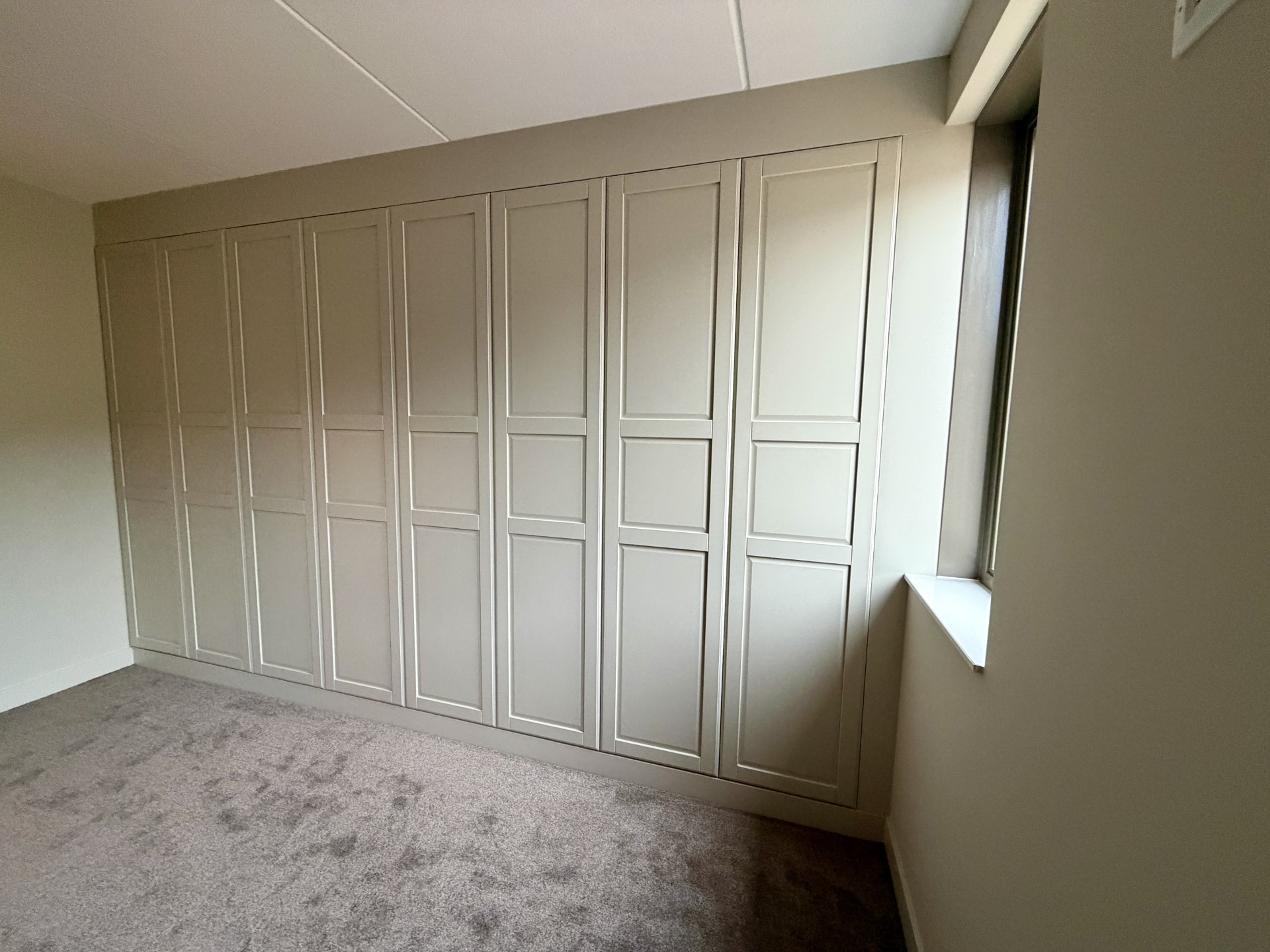 Strak afgewerkte inbouwkast op maat met paneeldeuren en meegeschilderde ombouw in dezelfde kleur als wand en plinten voor een luxe uitstraling.